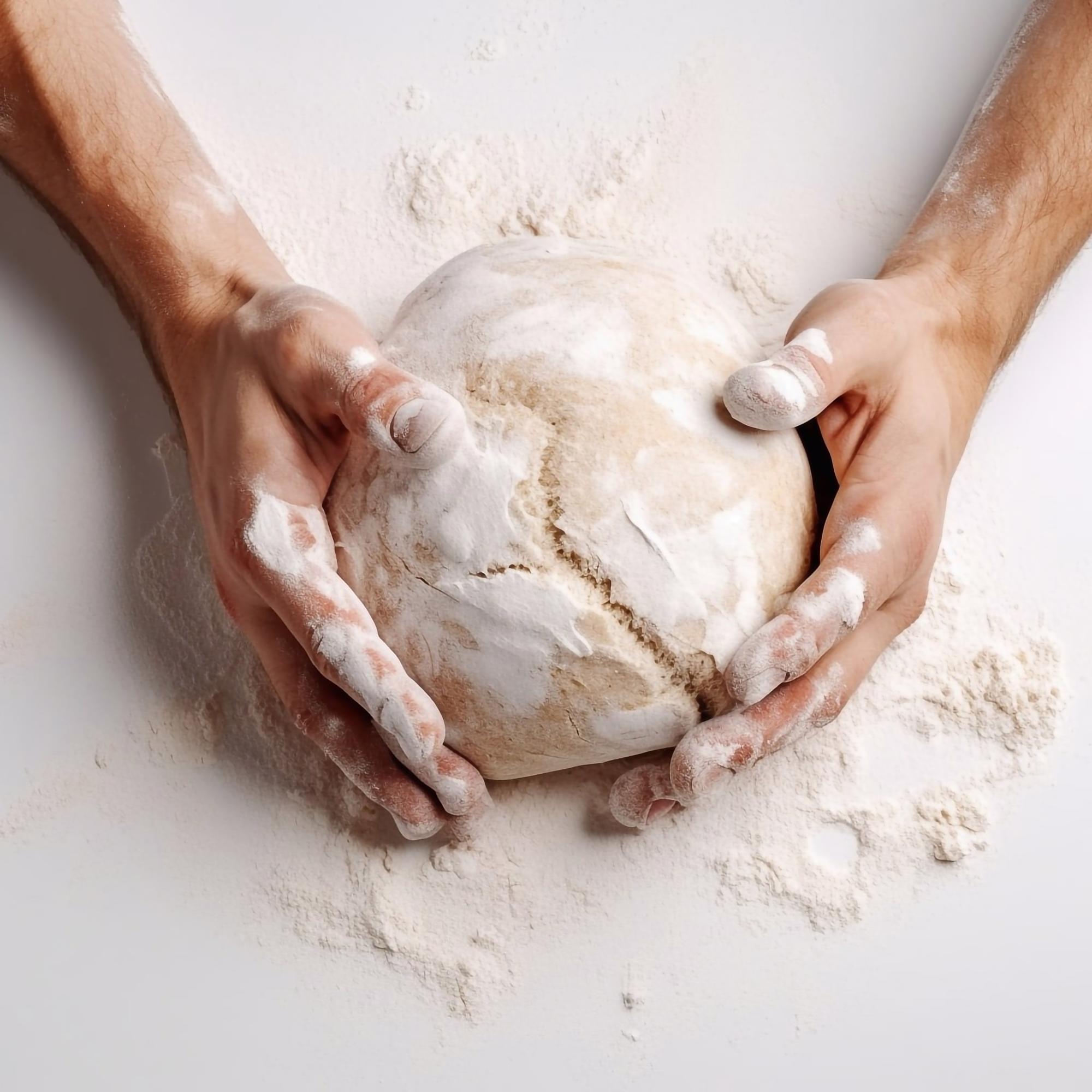 Close-up of hands kneading dough with flour on table